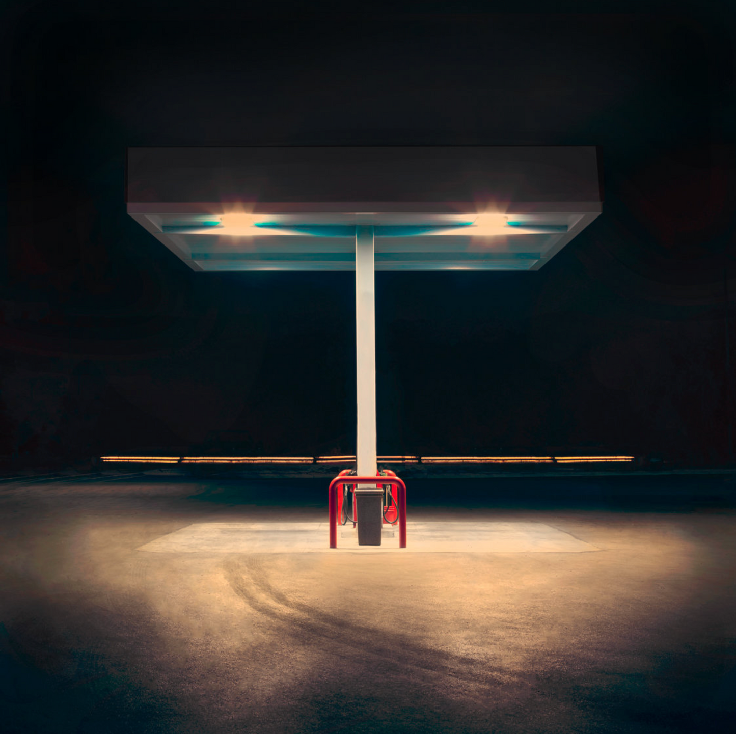 A photograph featuring a petrol station with a white pump and a red canopy, illuminated by the headlights of a car.