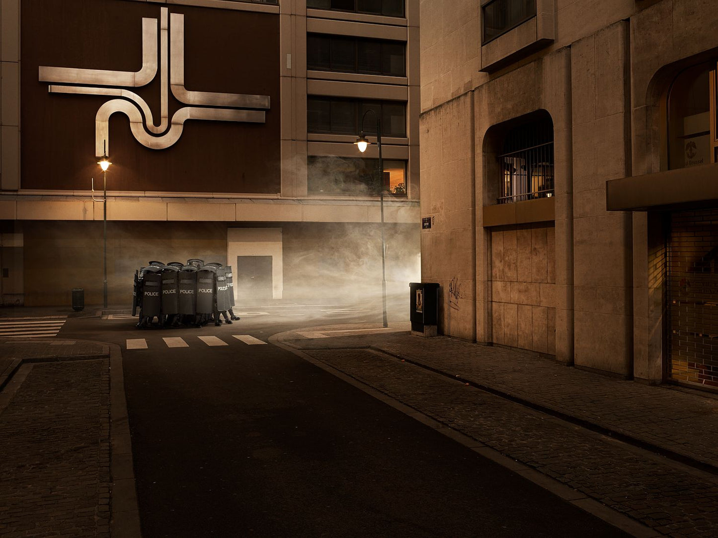 A photo of a street scene with riot police in the middle of the road showing a reflection of light and shadow on the pavement.