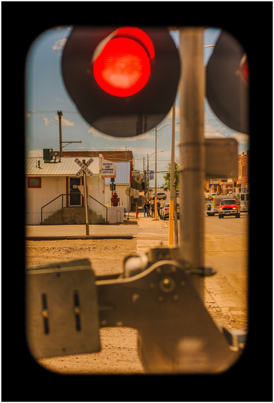 A framed photograph of a red train signal viewed from the window of a train, with a rural station in the background.