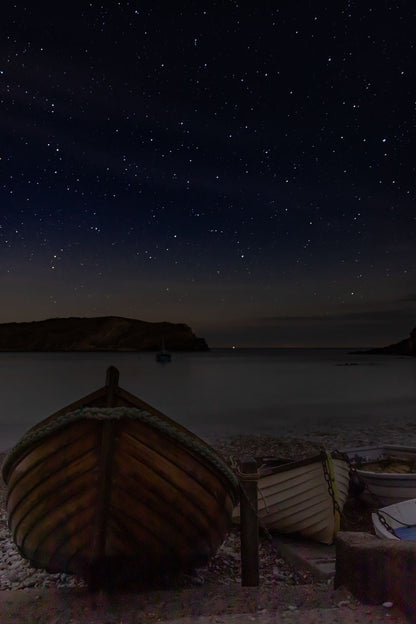 an image of a stary night with a boats in a shoreline and a ship on a body of water.