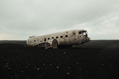 A photograph of a deteriorated airplane in a natural outdoor setting, with a cloudy sky in the background.