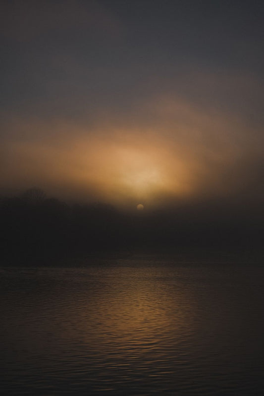 A photograph featuring a sunset over a body of water, with a warm glow over the landscape.