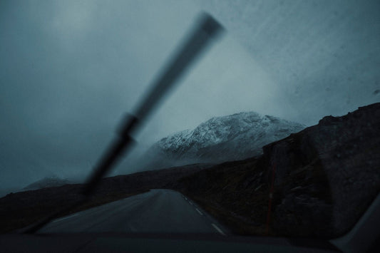 An image of a snow capped mountain taken from within a car on the road with a visible windshield wiper in view