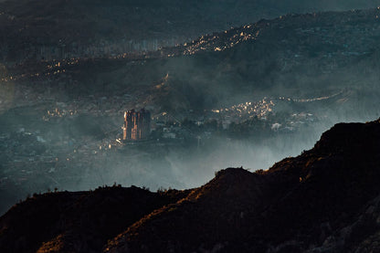 An image of a city in the mountains taken from a viewpoint. With fog in the foreground and a towering city block as the main focus of the image. 