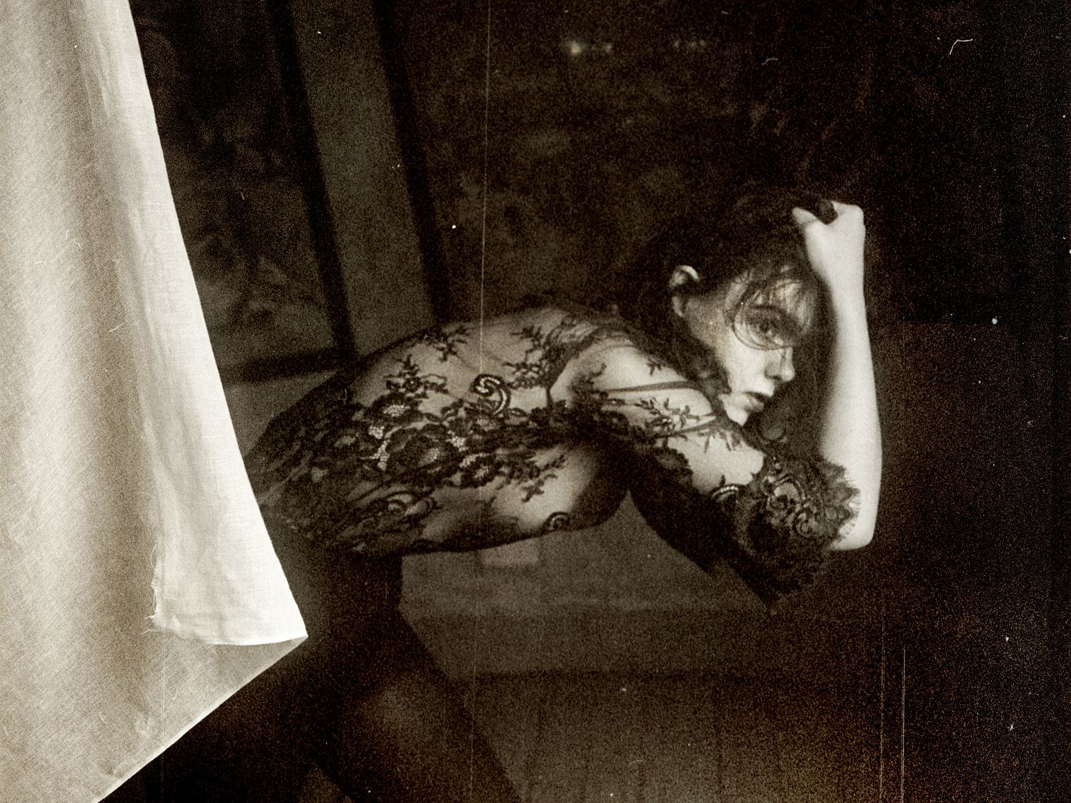 Black and white photograph of a woman with her hand behind her head, wearing a black dress with a floral pattern.