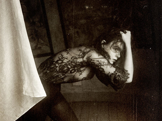 Black and white photograph of a woman with her hand behind her head, wearing a black dress with a floral pattern.