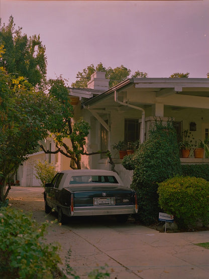 A fine art print featuring a classic car parked in front of a house with a warm-toned sunset in the background, displayed with a certificate of authenticity.