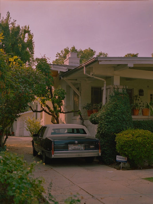 A fine art print featuring a classic car parked in front of a house with a warm-toned sunset in the background, displayed with a certificate of authenticity.