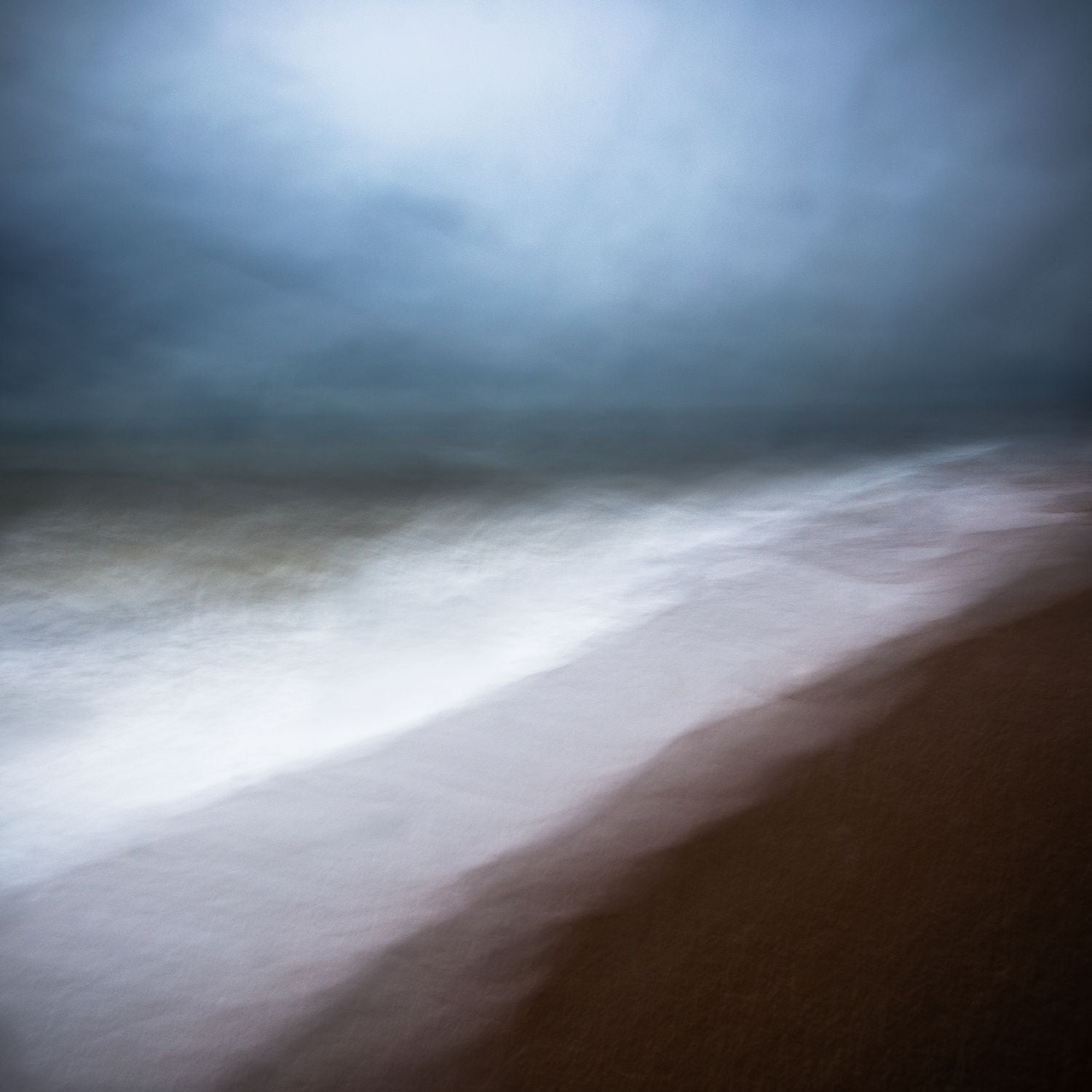 A fine art photograph featuring a dramatic coastal scene with dark clouds over the horizon and bright sky above the land.