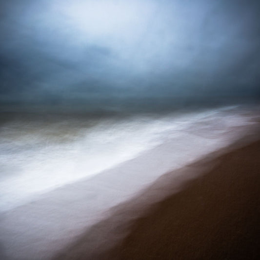 A fine art photograph featuring a dramatic coastal scene with dark clouds over the horizon and bright sky above the land.