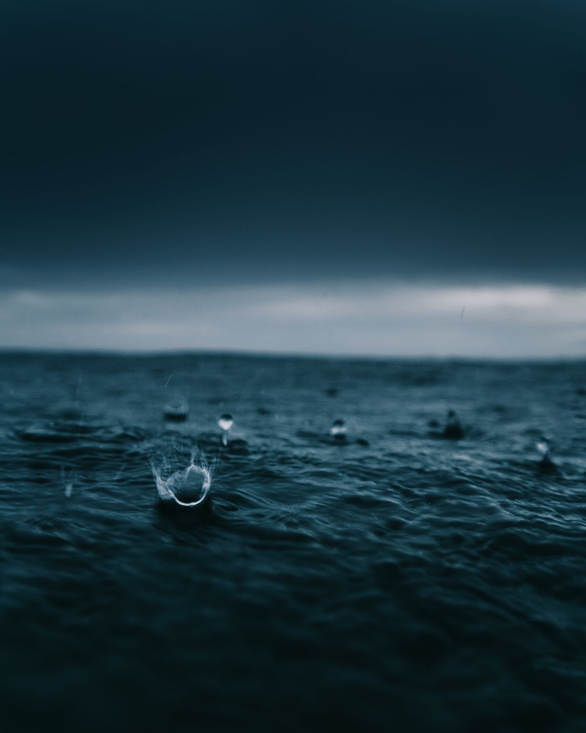 An image of raindrops hitting the surface of a waterbody with an artistic blue tint