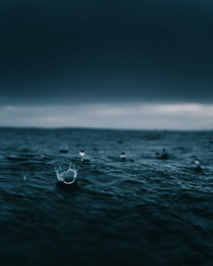 An image of raindrops hitting the surface of a waterbody with an artistic blue tint