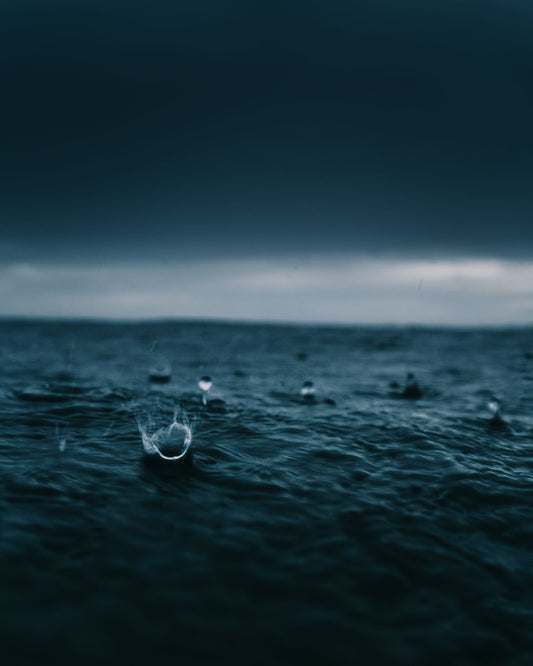 An image of raindrops hitting the surface of a waterbody with an artistic blue tint