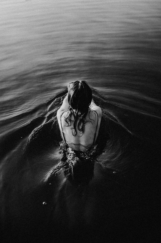 Black and white photo of a person floating in calm waters, reflecting on the surface.
