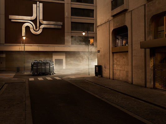 A photo of a street scene with riot police in the middle of the road showing a reflection of light and shadow on the pavement.
