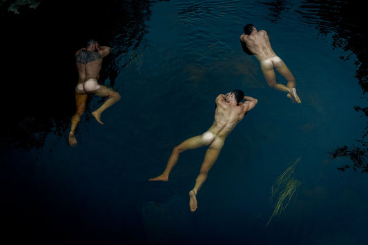An artistic photograph featuring three naked men in a body of water, viewed from above.