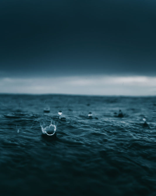 An image of raindrops hitting the surface of a waterbody with an artistic blue tint
