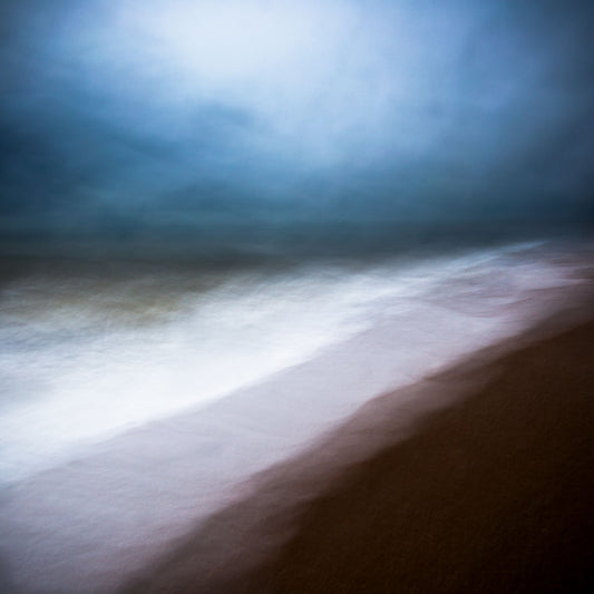 A fine art photograph featuring a dramatic coastal scene with dark clouds over the horizon and bright sky above the land.