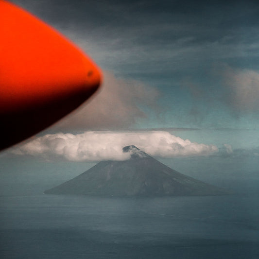 Artistic print featuring a dramatic sky with a prominent red object on the left and a volcanic landscape in the background, partially covered by clouds.