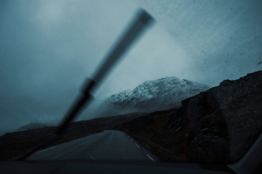 An image of a snow capped mountain taken from within a car on the road with a visible windshield wiper in view