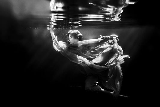 An artistic black and white image of a lady in white floating underwater 