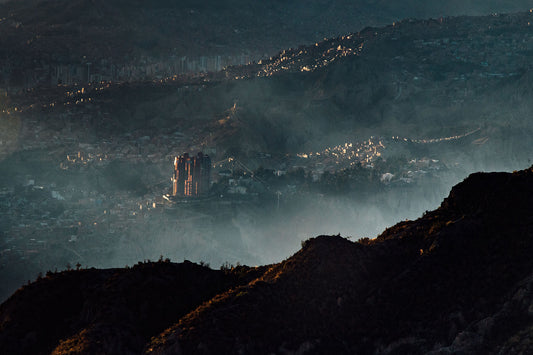 An image of a city in the mountains taken from a viewpoint. With fog in the foreground and a towering city block as the main focus of the image. 