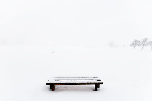 An image of a snow-covered bench with no visible features beyond the bench's silhouette.