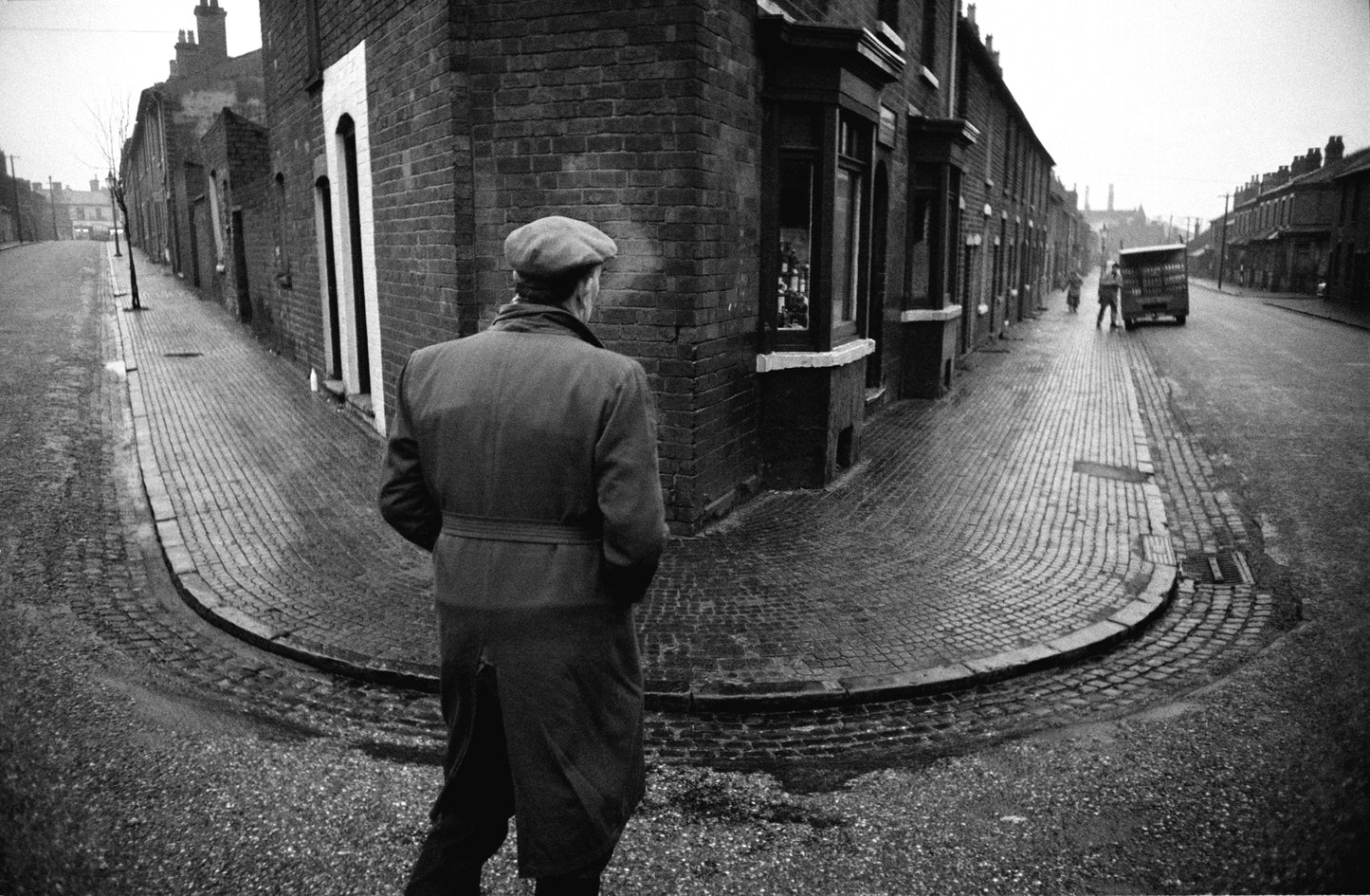 Black and white photograph of a street scene with a man standing on the sidewalk.