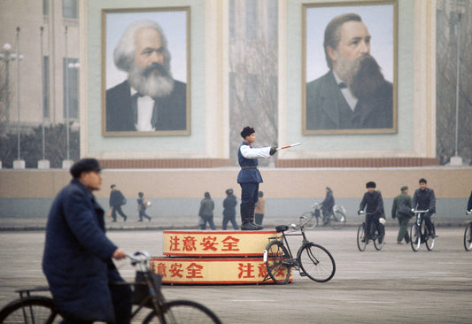 A photograph featuring a person standing on a platform with a banner, in front of a background that includes images of two men and a building.