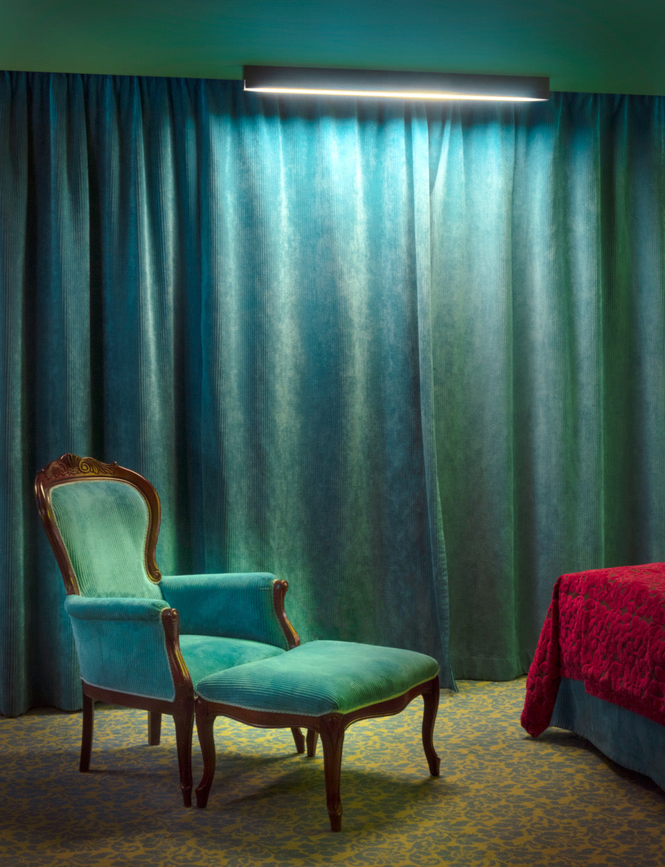 A framed and matted print featuring a blue upholstered chair in a room with green walls.