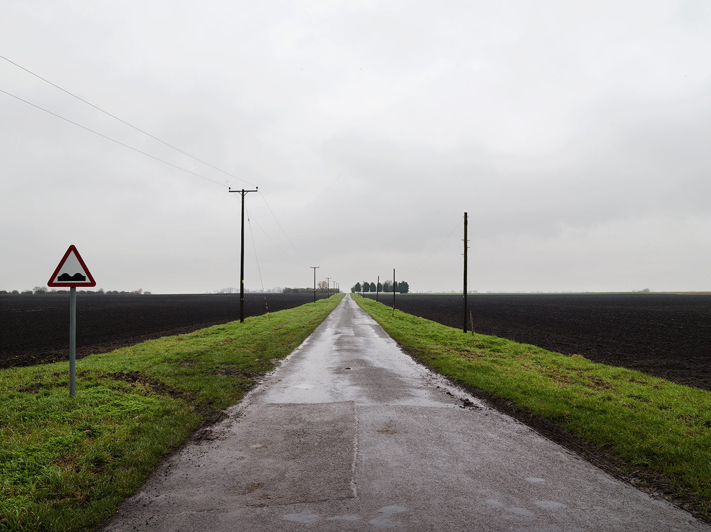 A landscape photograph featuring a wide road with power lines on either side, and a sky in the background. The foreground is green and misty, giving a sense of depth and atmosphere.