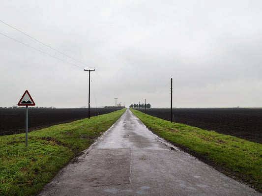 A landscape photograph featuring a wide road with power lines on either side, and a sky in the background. The foreground is green and misty, giving a sense of depth and atmosphere.
