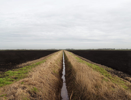 A photograph of an open farm land with a channel of water drawing a line in the middle