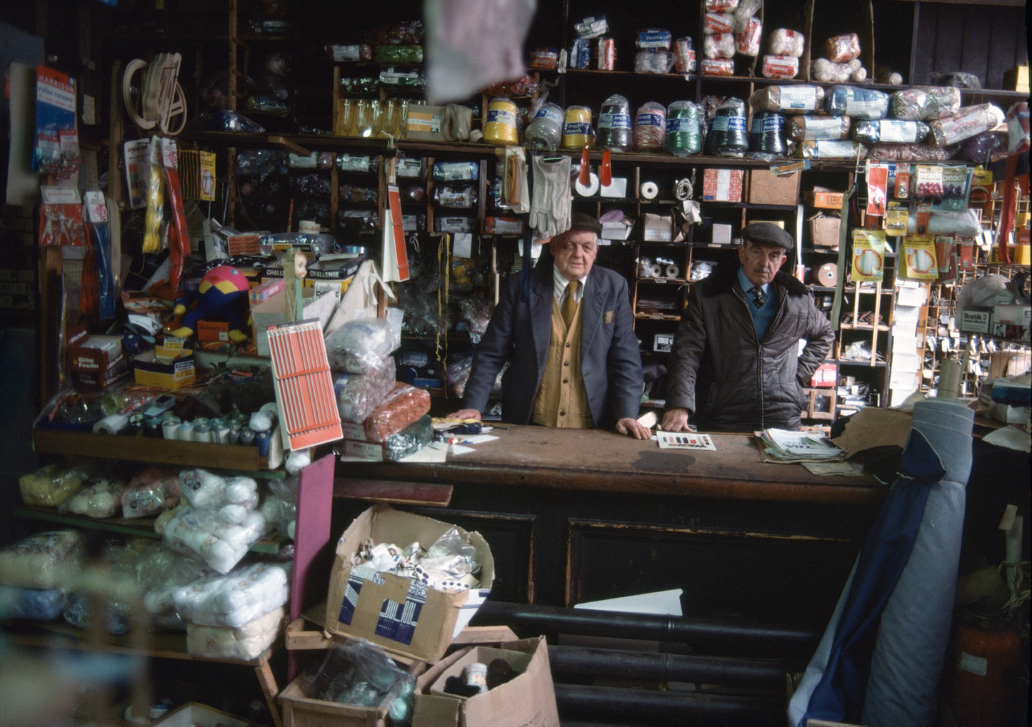 A photograph of two men standing in a grocery store aisle, with various items on the shelves and counters in the background.