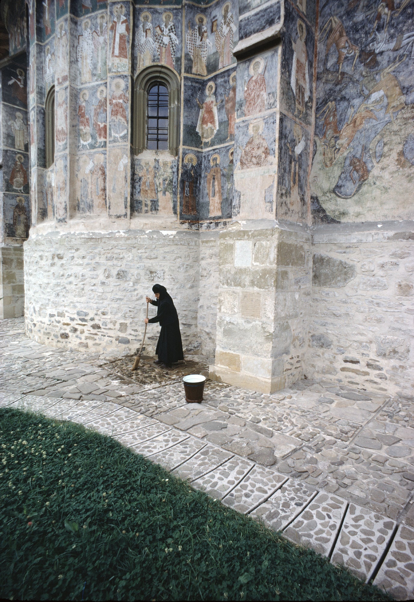 A nun dressed in black sweeping the courtyard of a church