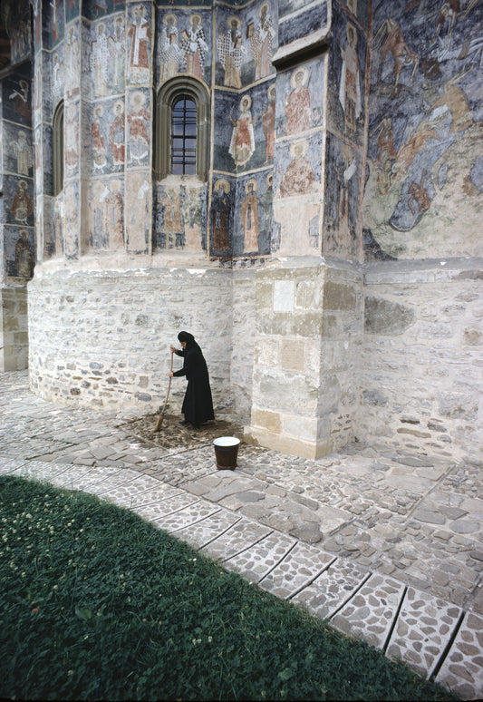 A nun dressed in black sweeping the courtyard of a church
