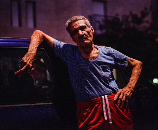 An image of a person standing with their hand on a car door, looking off to the distance.