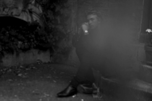 A black and white image of a person seated outdoors with a blurred background.