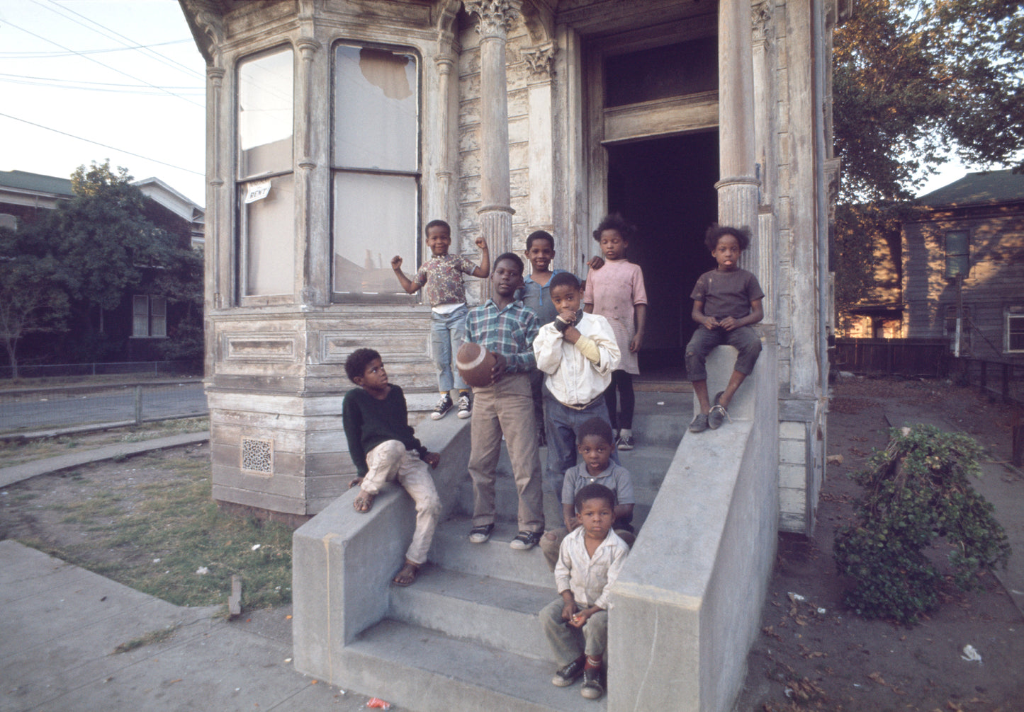 A photograph of children standing outside house, with one holding a football