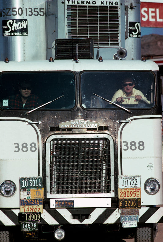 An image of two men driving in a white truck
