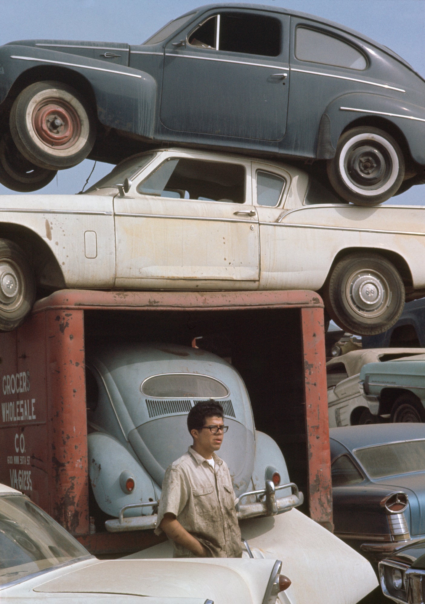 A photograph of a  mechanic standing in front of a stack of old cars