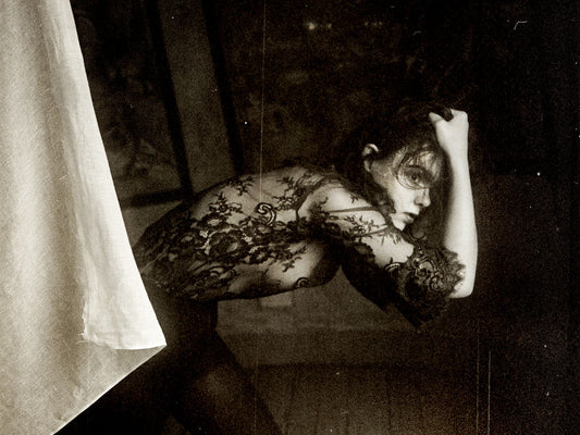 Black and white photograph of a woman with her hand behind her head, wearing a black dress with a floral pattern.
