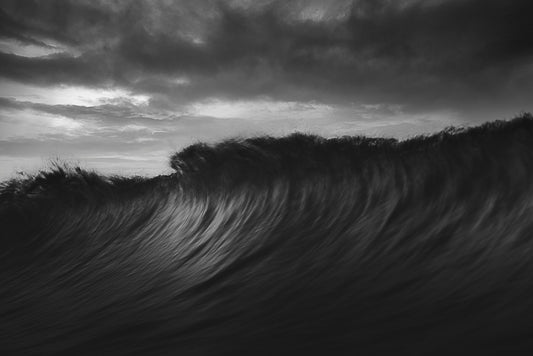 A black and white image of a large wave in the ocean, with a visible white border for mounting.
