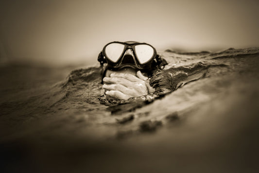 A black and white photograph of a person swimming with their goggle on top of their head and their hand whipping the face