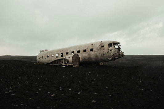 A photograph of a deteriorated airplane in a natural outdoor setting, with a cloudy sky in the background.