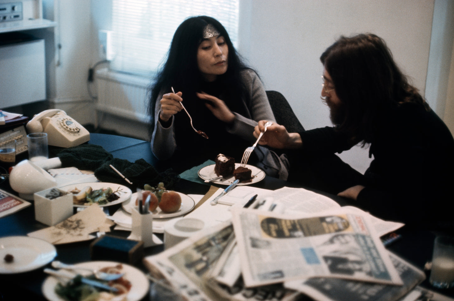 A photograph showing two people seated at a table with food and newspapers, engaged in a heated discussion.