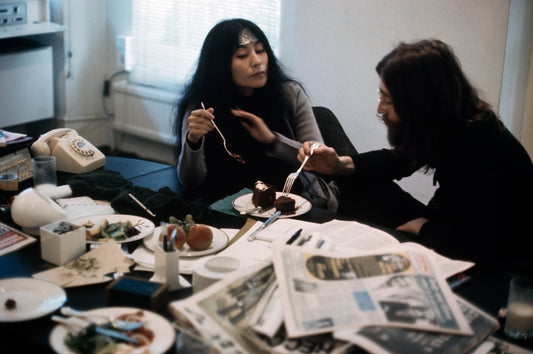 A photograph showing two people seated at a table with food and newspapers, engaged in a heated discussion.